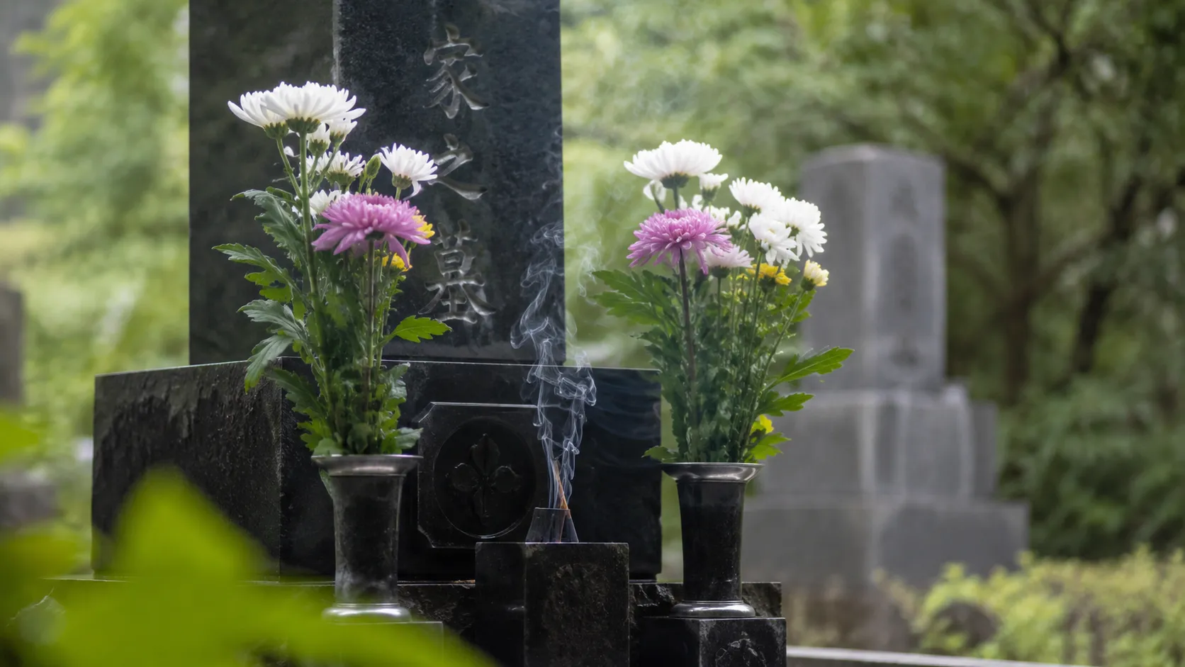 線香の煙がたつ墓前に、白とピンクの花が供えられている様子